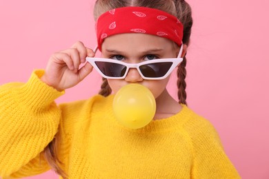 Photo of Girl in sunglasses blowing bubble gum on pink background