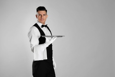 Photo of Handsome butler with tray on light grey background, space for text