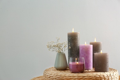 Photo of Different candles on wicker table against light grey background. Space for text