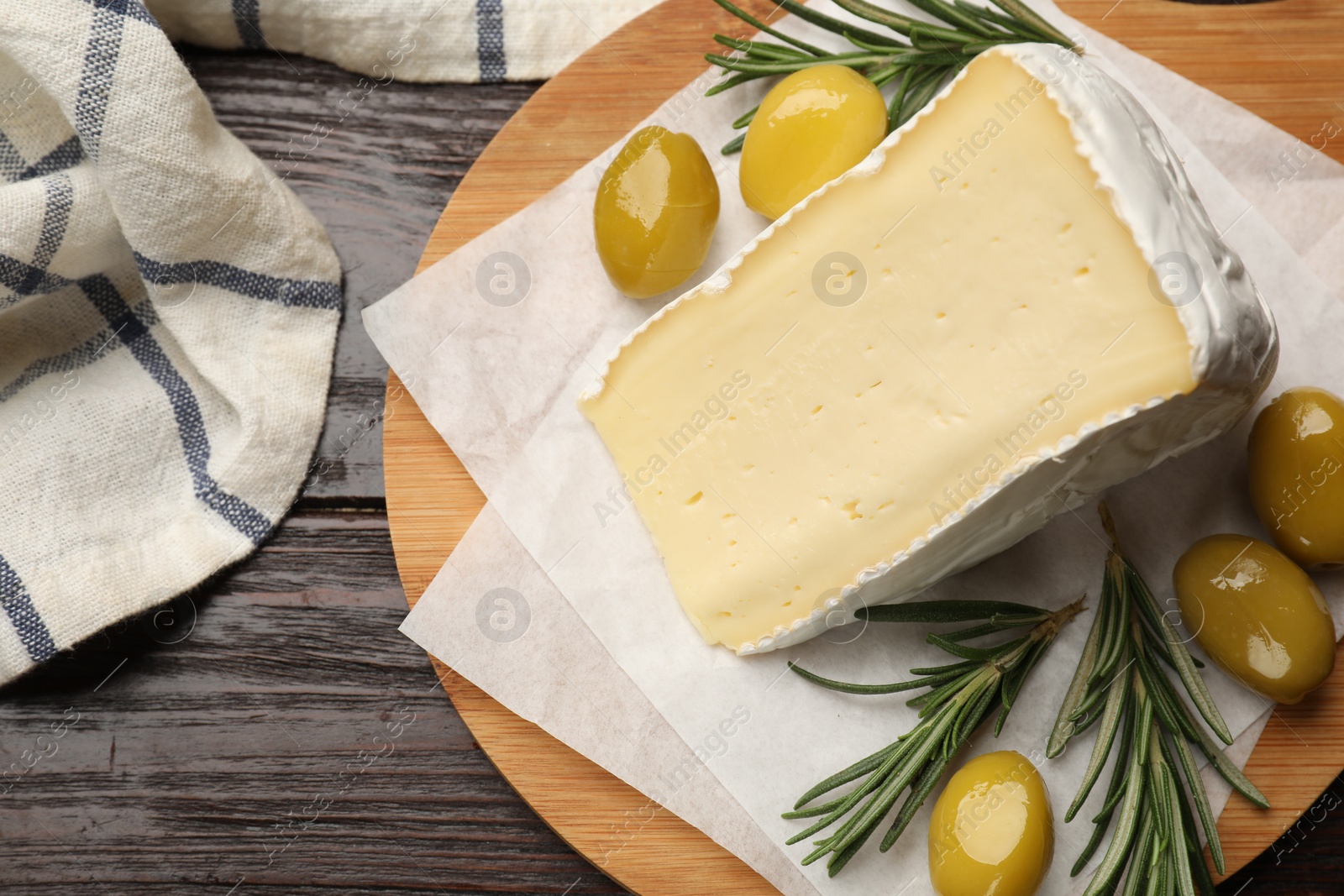 Photo of Board with piece of tasty camembert cheese, olives and rosemary on wooden table, top view