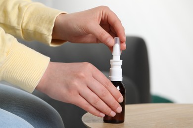 Photo of Woman with nasal spray at wooden table indoors, closeup
