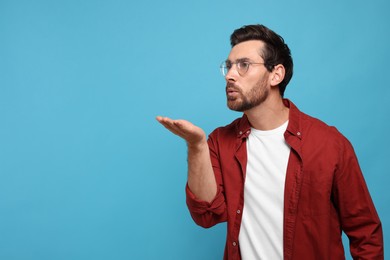 Photo of Handsome man blowing kiss on light blue background. Space for text