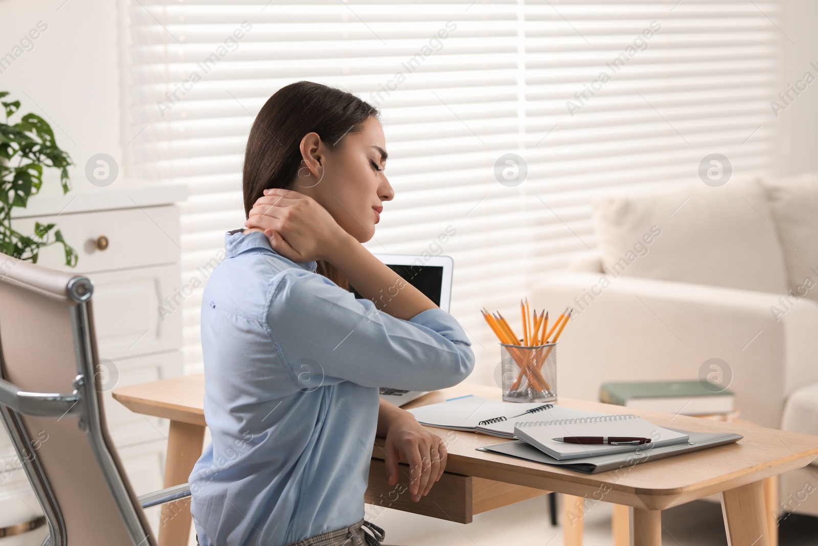 Photo of Young woman suffering from neck pain at table in office