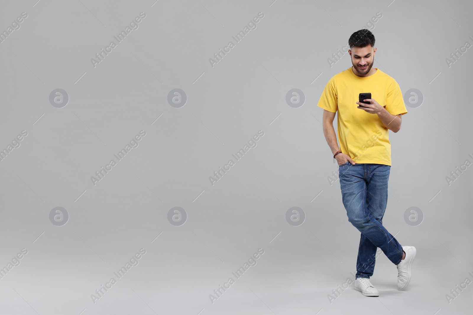 Photo of Handsome young man using smartphone on grey background, space for text