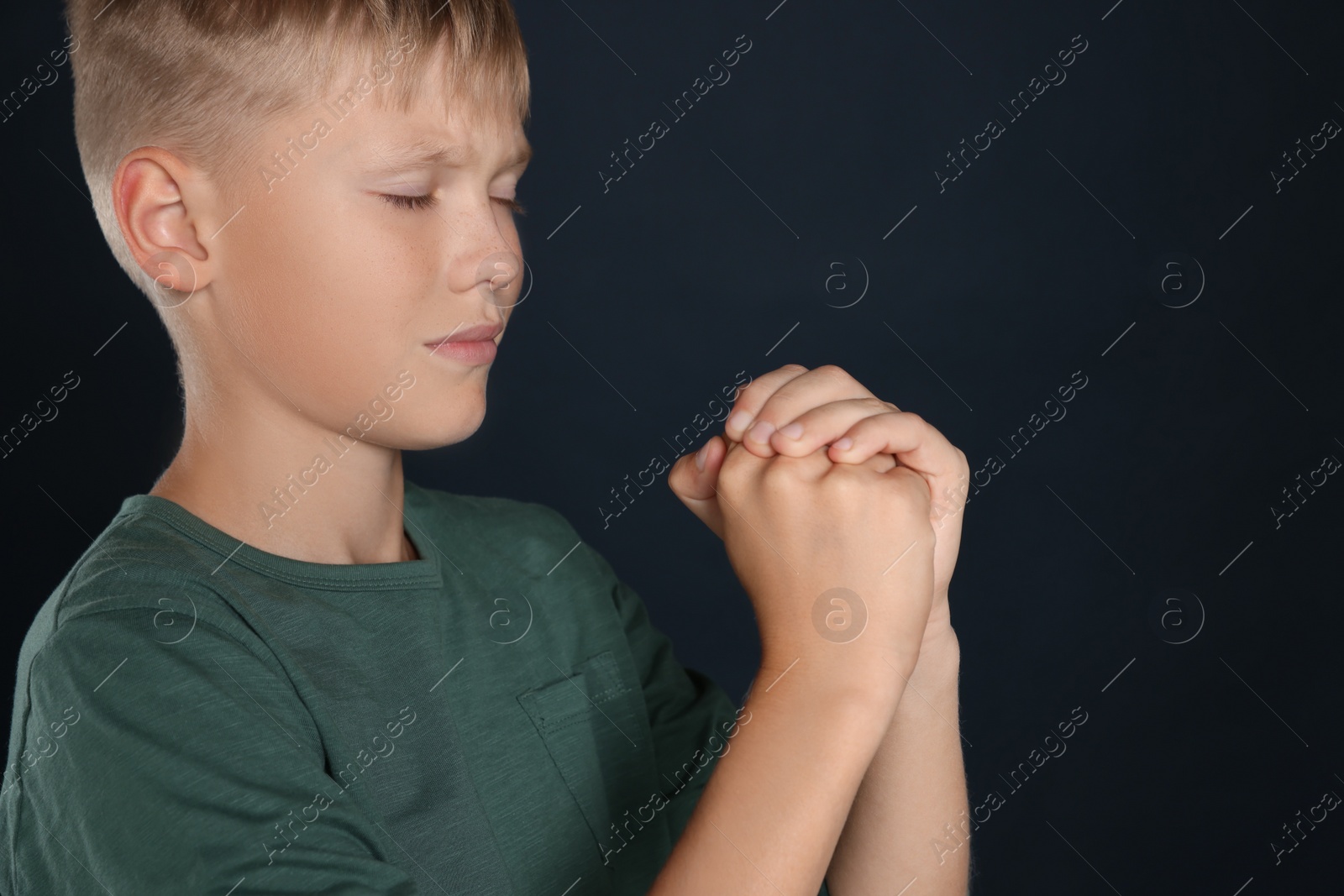 Photo of Boy with clasped hands praying on black background, space for text