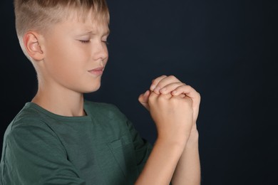 Photo of Boy with clasped hands praying on black background, space for text