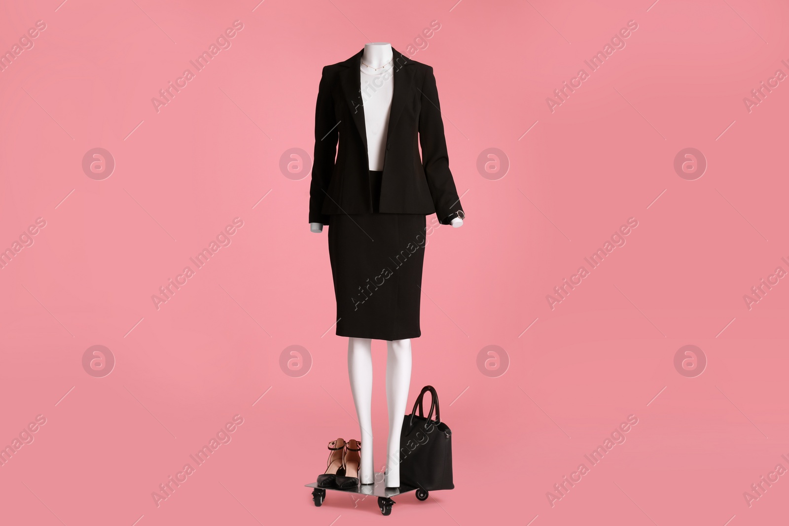 Photo of Female mannequin with accessories and shoes dressed in black classic suit on pink background. Stylish outfit