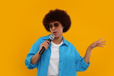 Photo of Curly young woman in sunglasses with microphone singing on yellow background