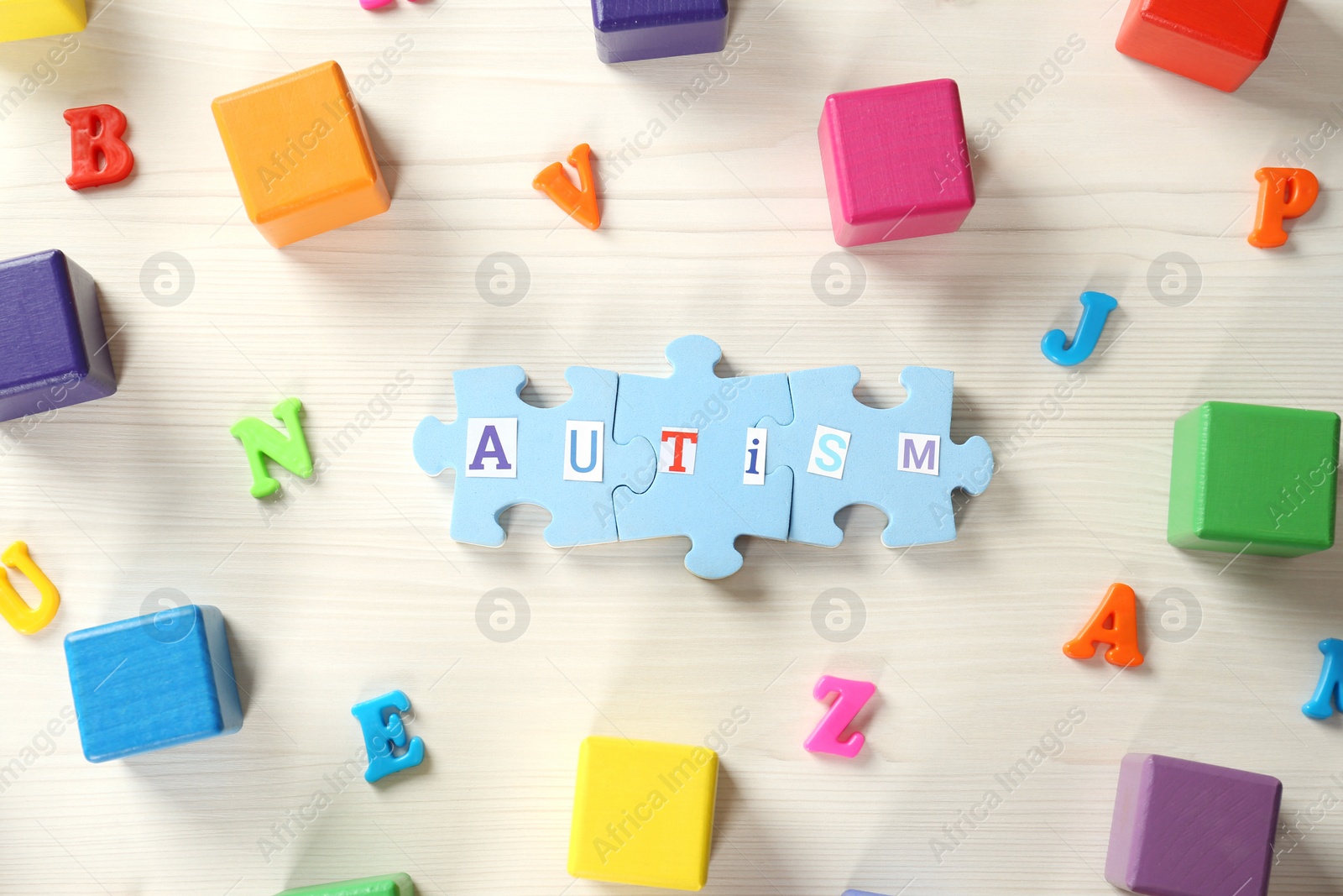 Photo of Word Autism made of puzzle pieces, colorful cubes and letters on white wooden table, flat lay