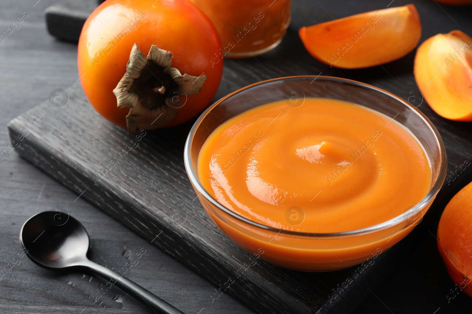 Photo of Delicious persimmon jam in bowl served on dark gray wooden table, closeup