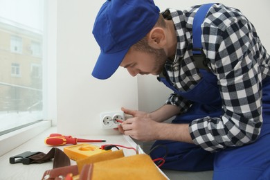 Photo of Electrician with screwdriver repairing power socket indoors