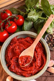 Bowl of tasty tomato paste with spoon and ingredients on wooden table, flat lay
