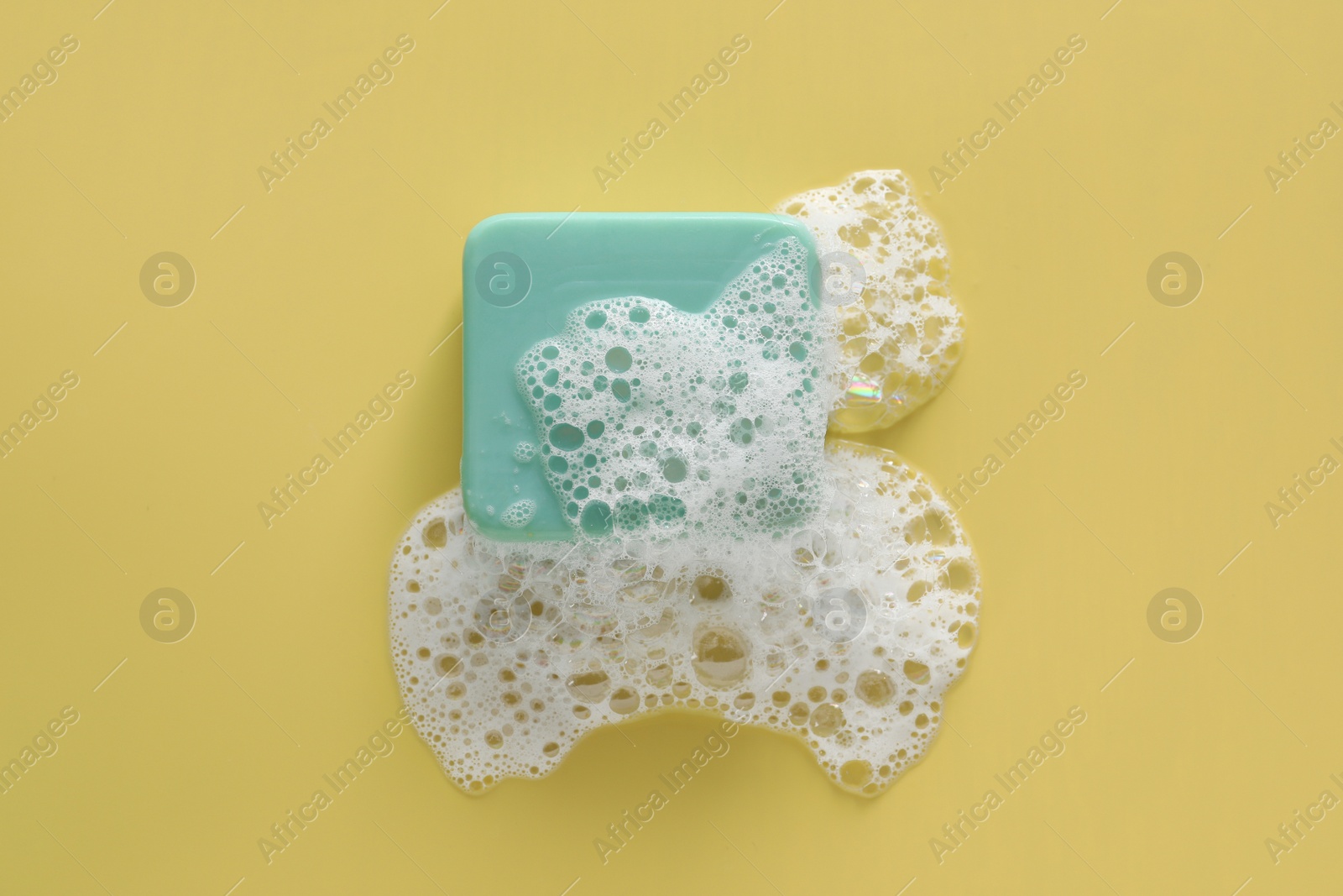 Photo of Soap bar with fluffy foam on yellow background, top view