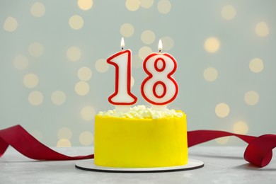 Photo of Coming of age party - 18th birthday. Delicious cake with number shaped candles on white table against blurred lights