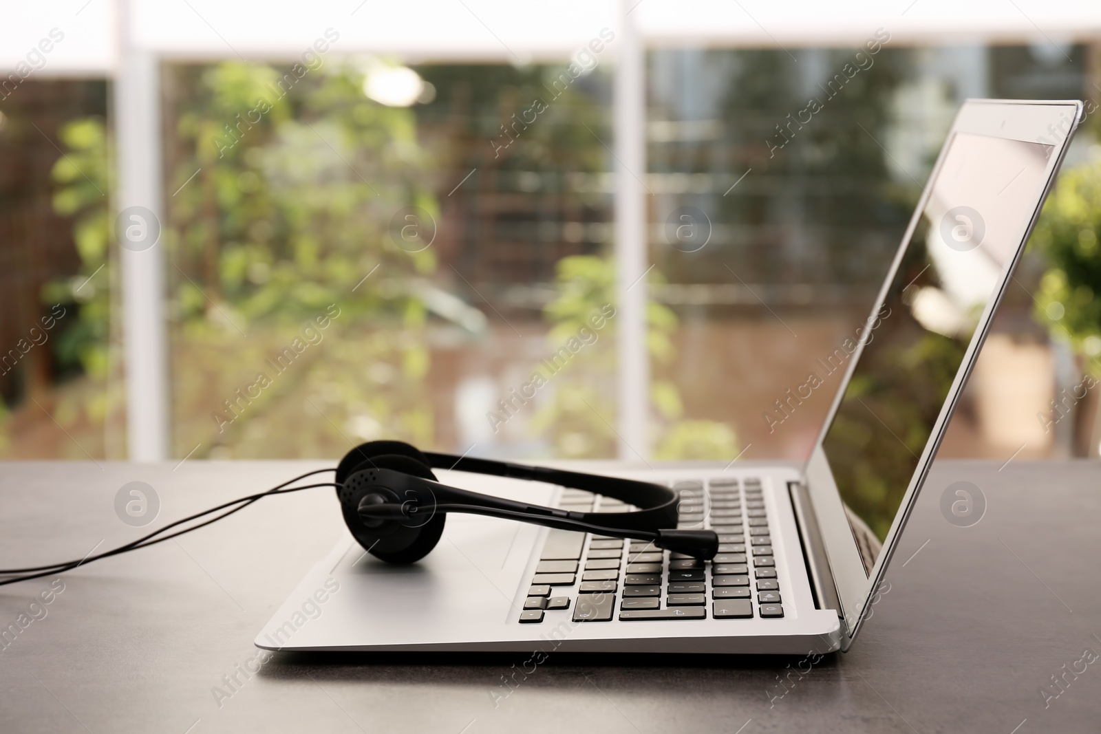 Photo of Modern laptop and headset on table indoors. Technical support concept