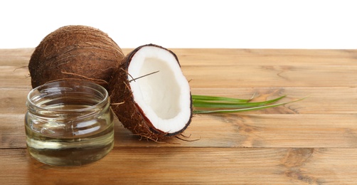 Photo of Ripe coconuts and jar with natural organic oil on wooden table against white background