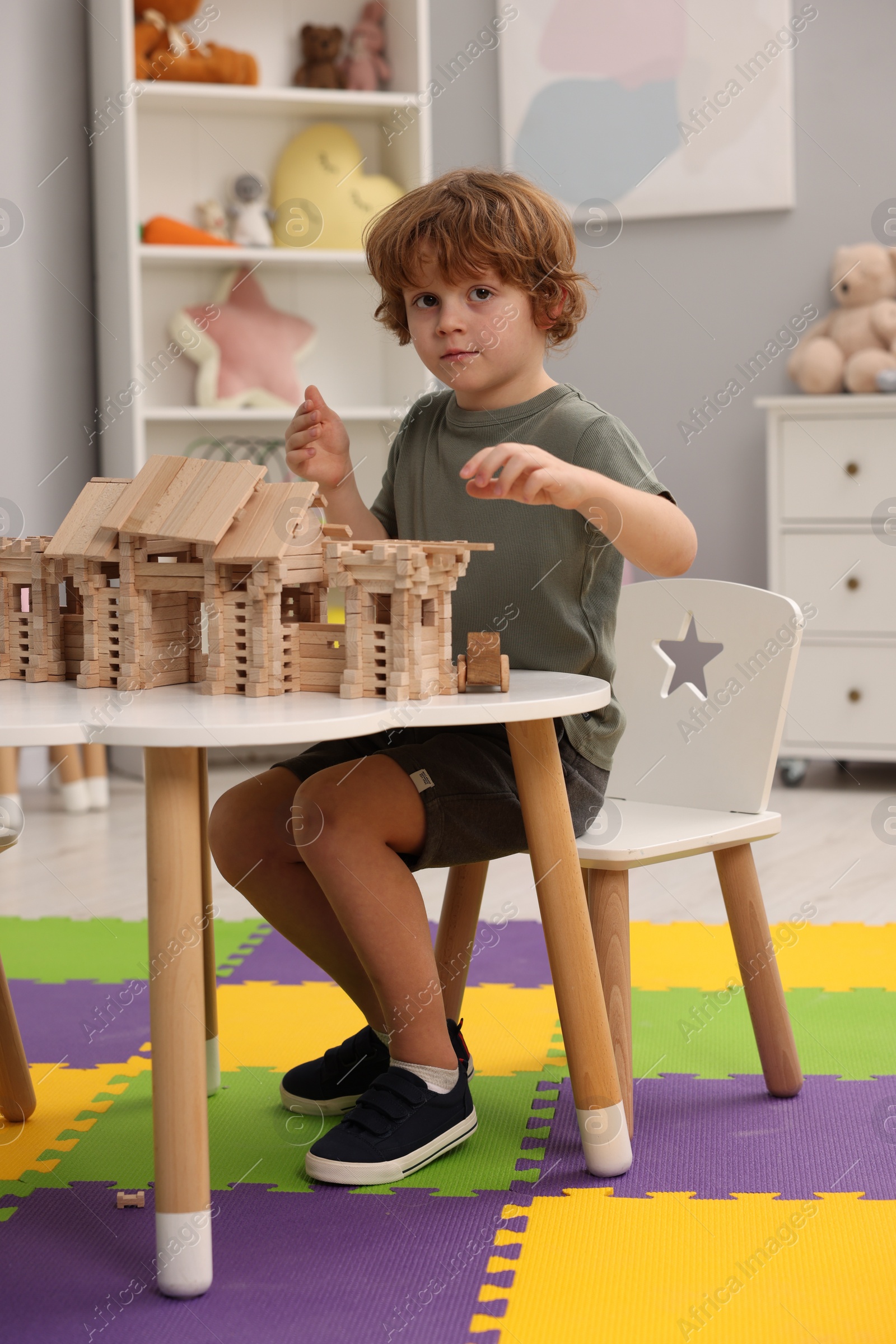 Photo of Little boy playing with wooden entry gate at white table in room. Child's toy