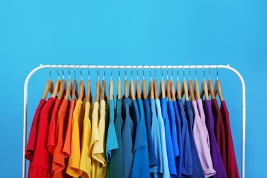 Rack with bright clothes on blue background. Rainbow colors