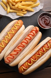 Photo of Delicious hot dogs with sauces and French fries on wooden table, top view