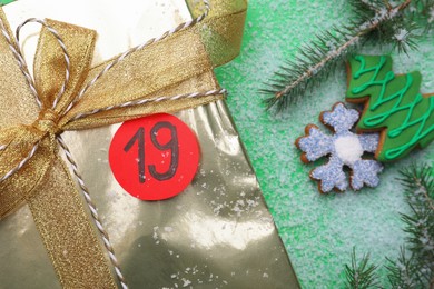 Gift box with paper tag and gingerbread cookies on green background, flat lay. December, 19 - Saint Nicholas Day