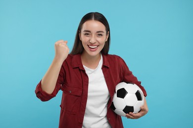 Happy fan holding soccer ball and celebrating on light blue background