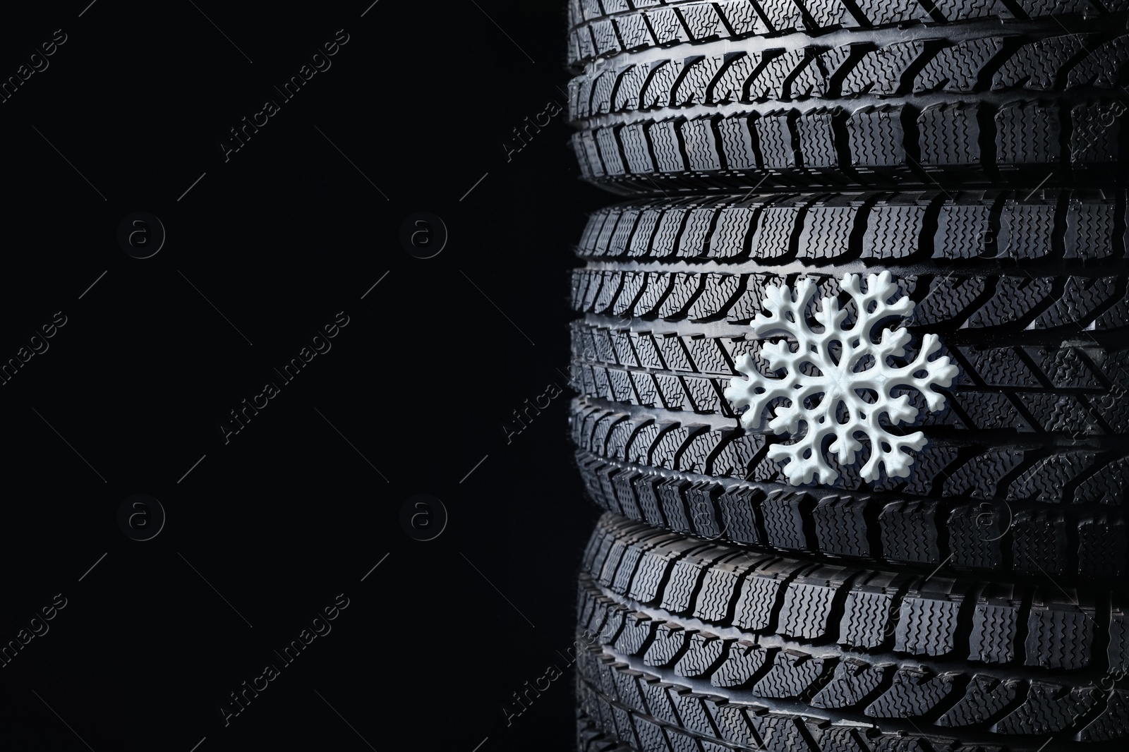 Image of Stacked winter tires with snowflake on black background, closeup. Space for text