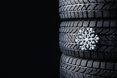 Image of Stacked winter tires with snowflake on black background, closeup. Space for text