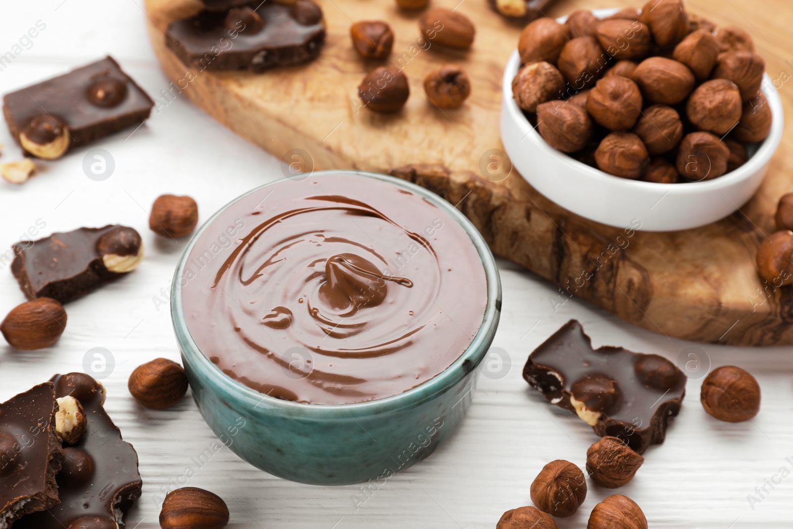 Photo of Bowl with tasty paste, chocolate pieces and nuts on white wooden table