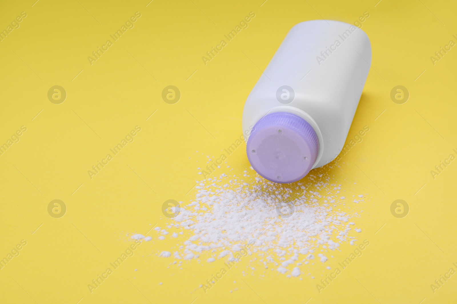 Photo of Bottle and scattered dusting powder on yellow background, space for text. Baby cosmetic product