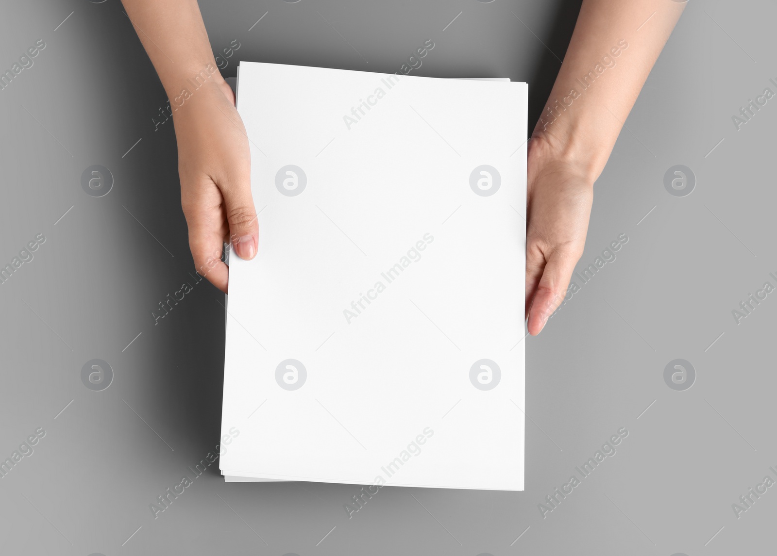 Photo of Woman holding blank paper sheets for brochure at grey table, top view. Mock up