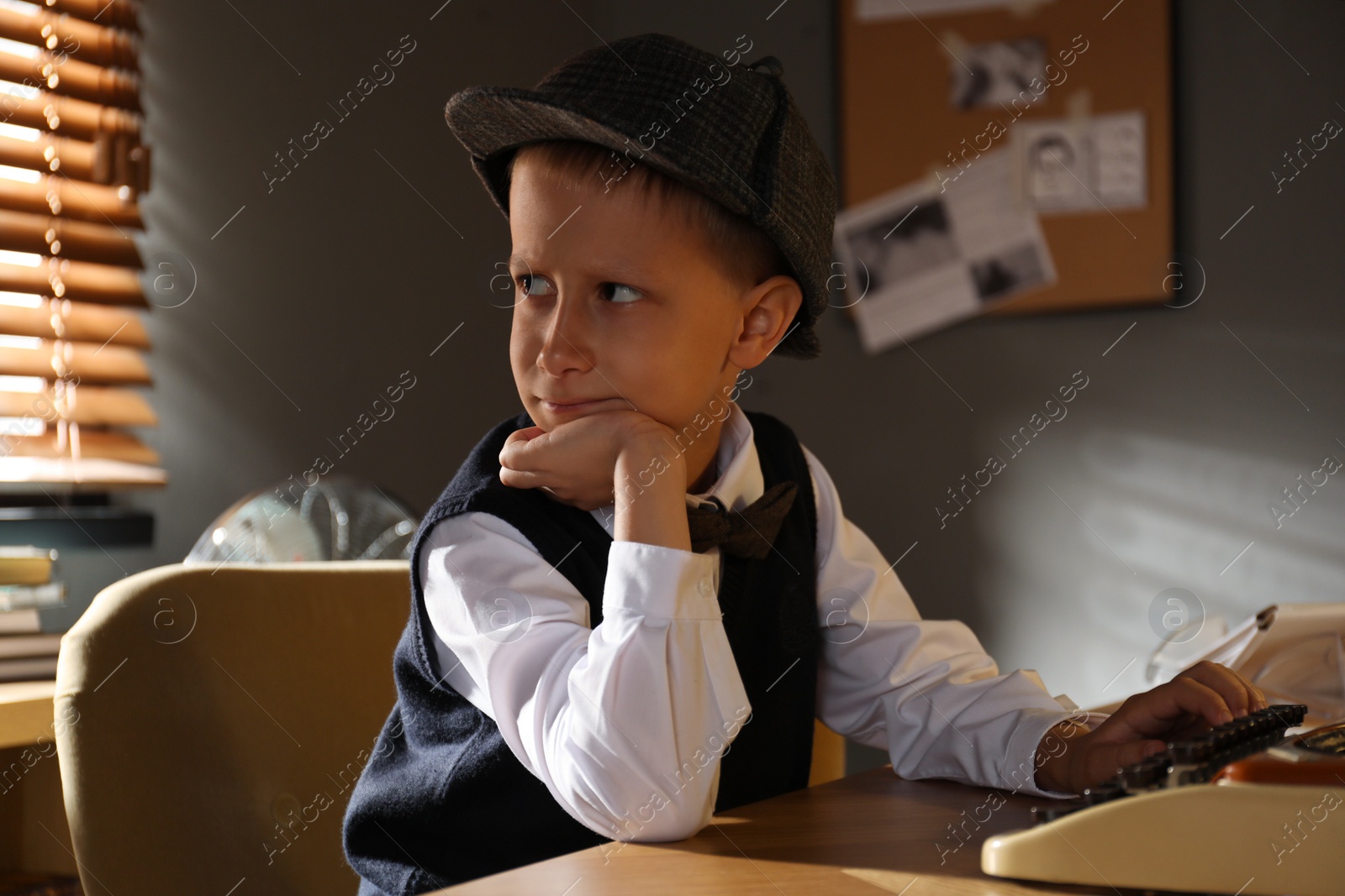 Photo of Cute little detective using typewriter at table in office