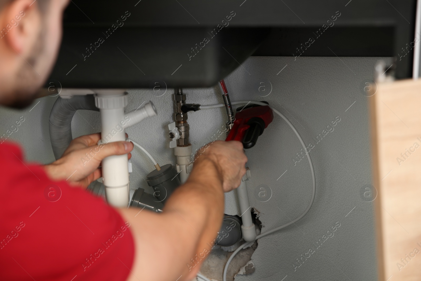 Photo of Male plumber repairing kitchen sink with pipe wrench, closeup