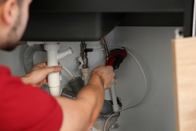 Male plumber repairing kitchen sink with pipe wrench, closeup