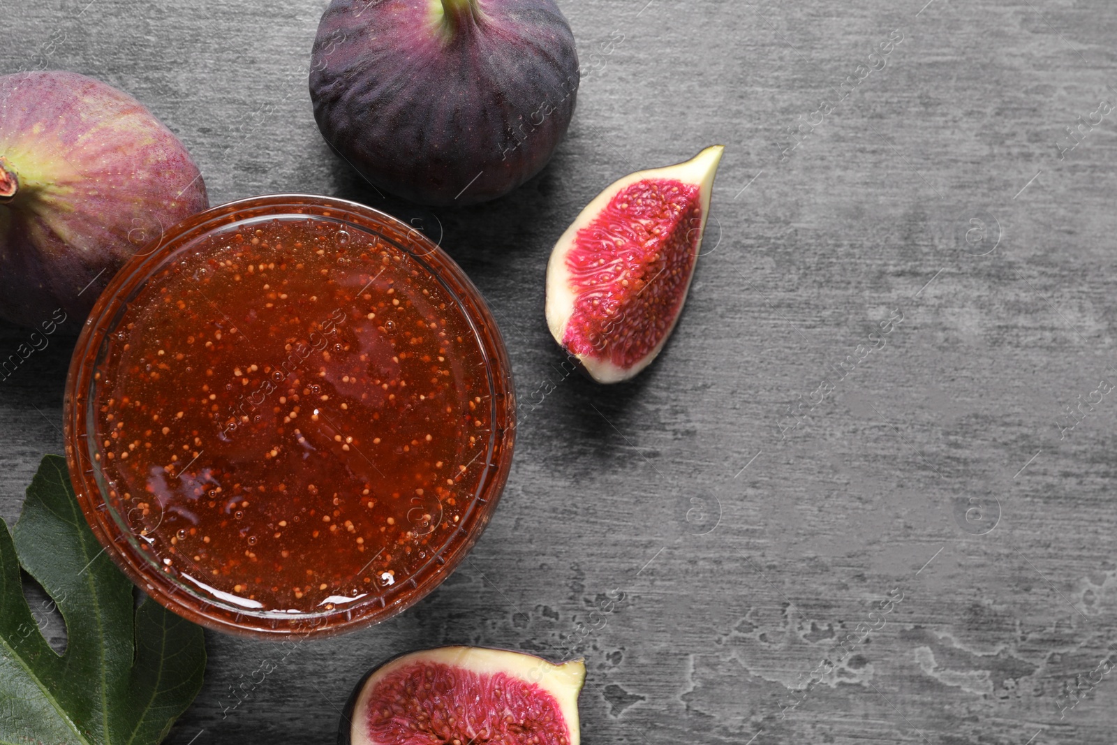 Photo of Bowl with tasty sweet jam and fresh figs on grey table, flat lay. Space for text