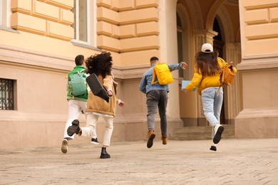 Photo of Being late. Group of students running towards building outdoors, back view