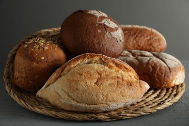 Photo of Wicker basket with different types of fresh bread on grey wooden table, closeup