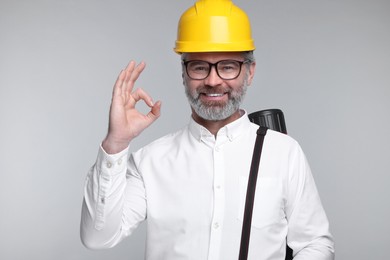 Photo of Architect in hard hat with drawing tube showing ok gesture on grey background