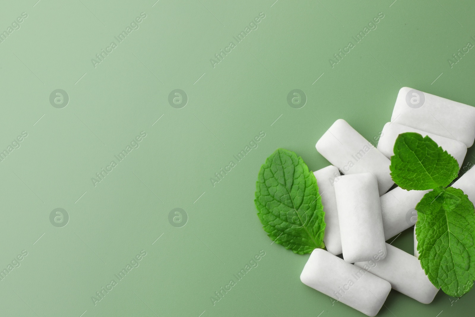 Photo of Tasty white chewing gums and mint leaves on light green background, top view. Space for text