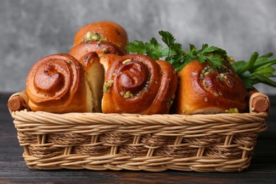 Photo of Delicious pampushky (buns with garlic) in wicker basket on wooden table, closeup