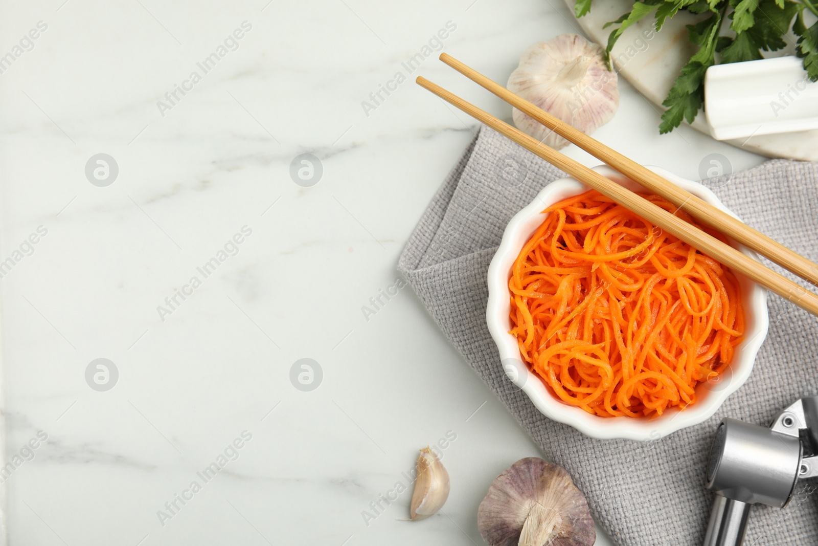 Photo of Delicious Korean carrot salad, garlic and parsley on white marble table, flat lay. Space for text