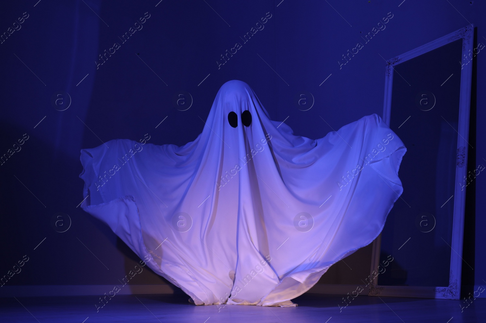 Photo of Creepy ghost. Woman covered with sheet in blue light