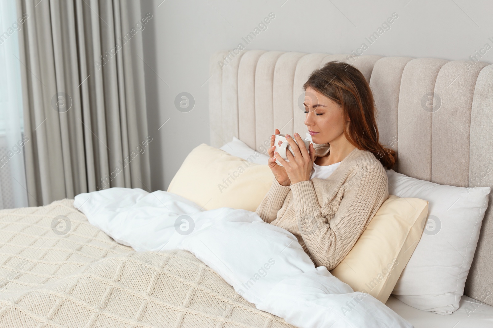 Photo of Beautiful woman with cup of drink in bed at home