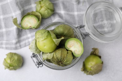 Photo of Fresh green tomatillos with husk in glass jar on light table, flat lay