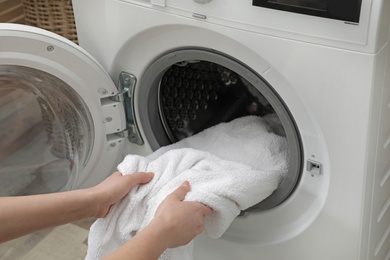 Photo of Woman taking clean towel from washing machine in laundry room, closeup