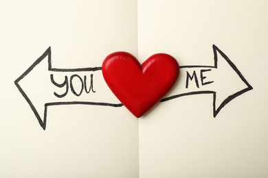 Photo of Heart between arrows with words YOU and ME pointing in different directions on notepad, top view. Composition symbolizing relationship problems