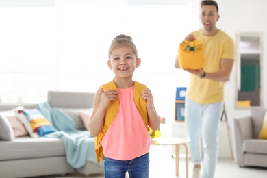 Young man reminding his little child to take lunch bag as she leaving for school