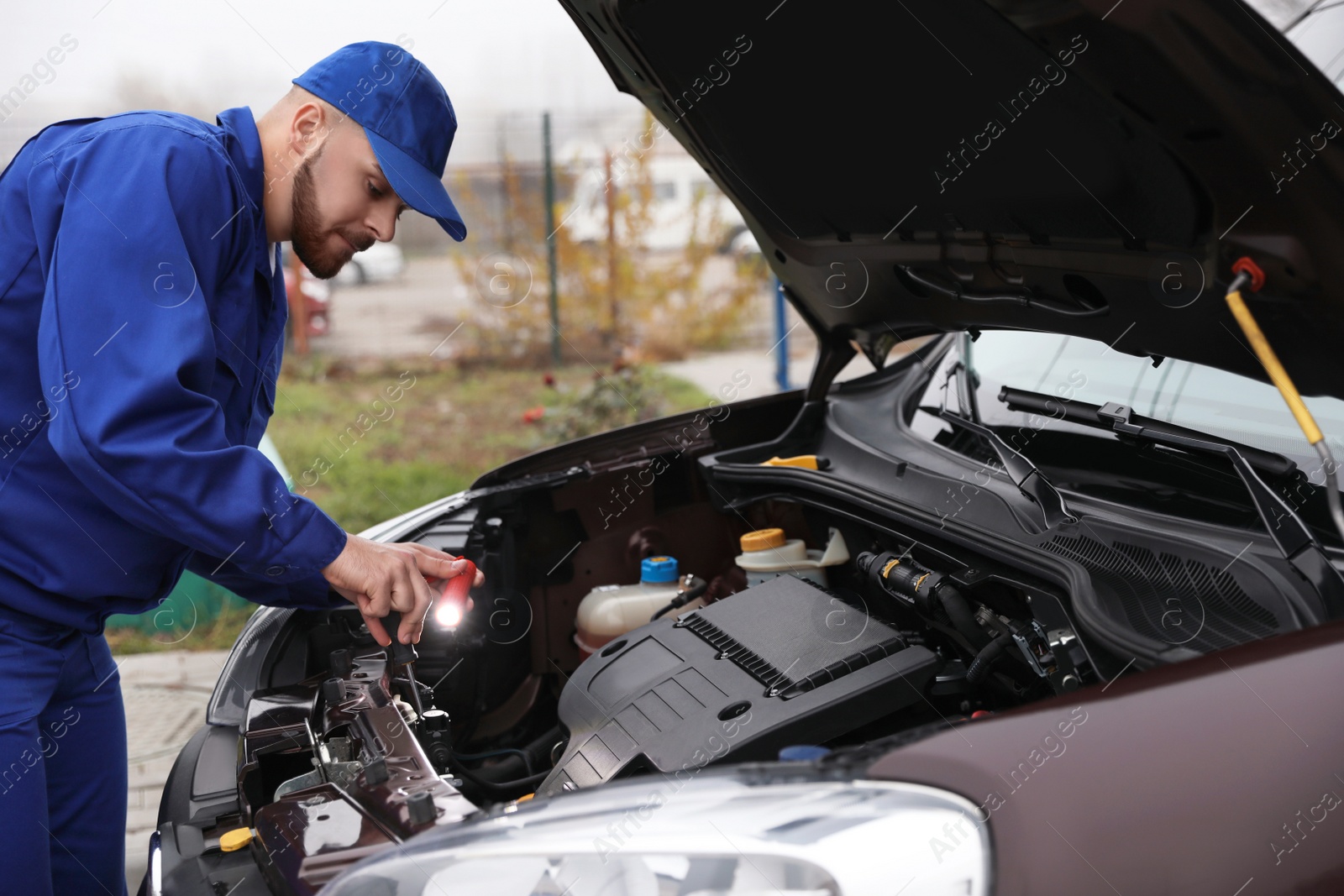 Photo of Young mechanic with flashlight fixing car outdoors