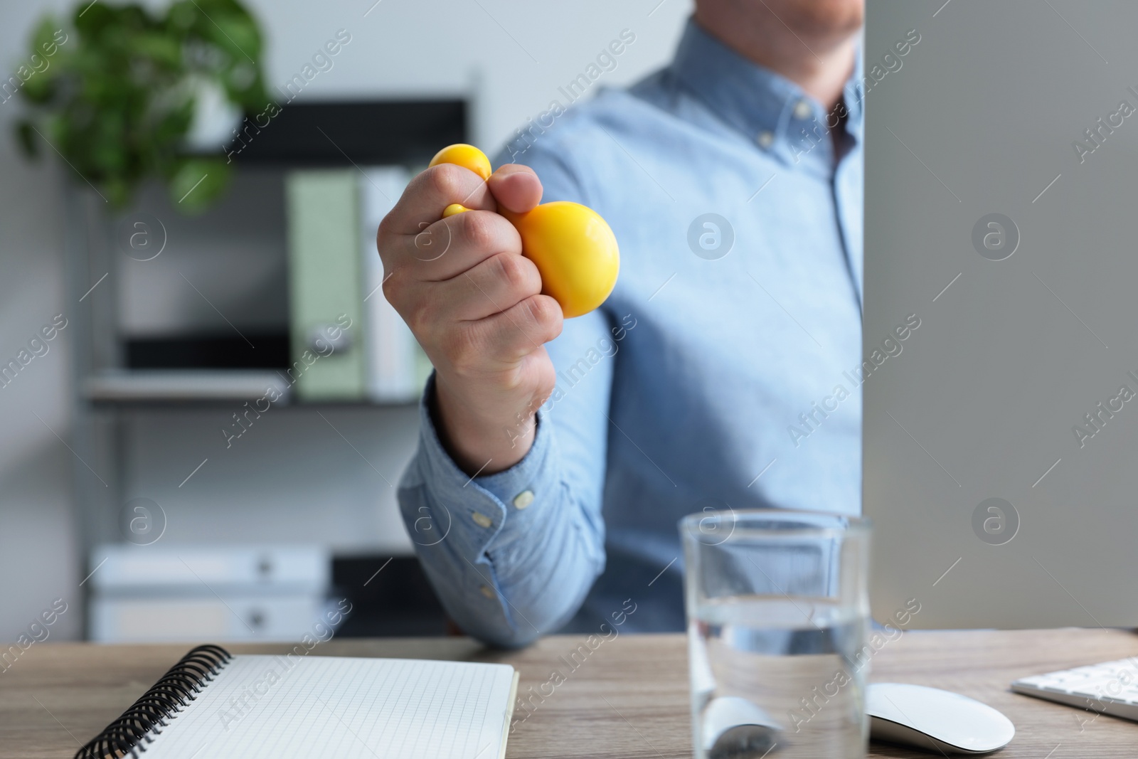 Photo of Man squeezing antistress ball while working with computer in office, closeup