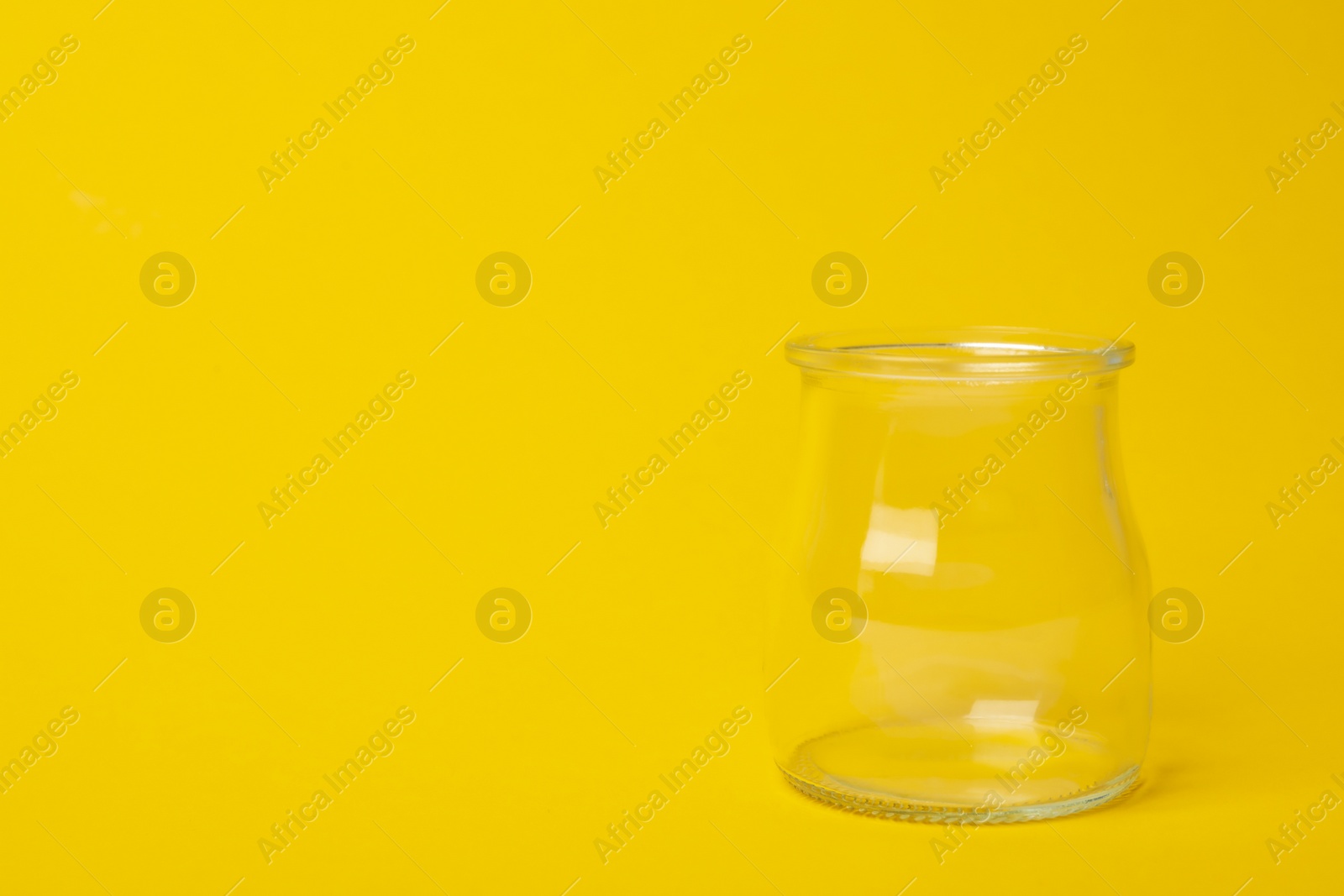 Photo of Open empty glass jar on yellow background, space for text