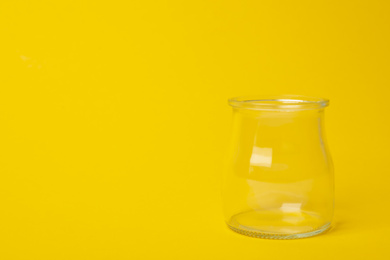 Photo of Open empty glass jar on yellow background, space for text